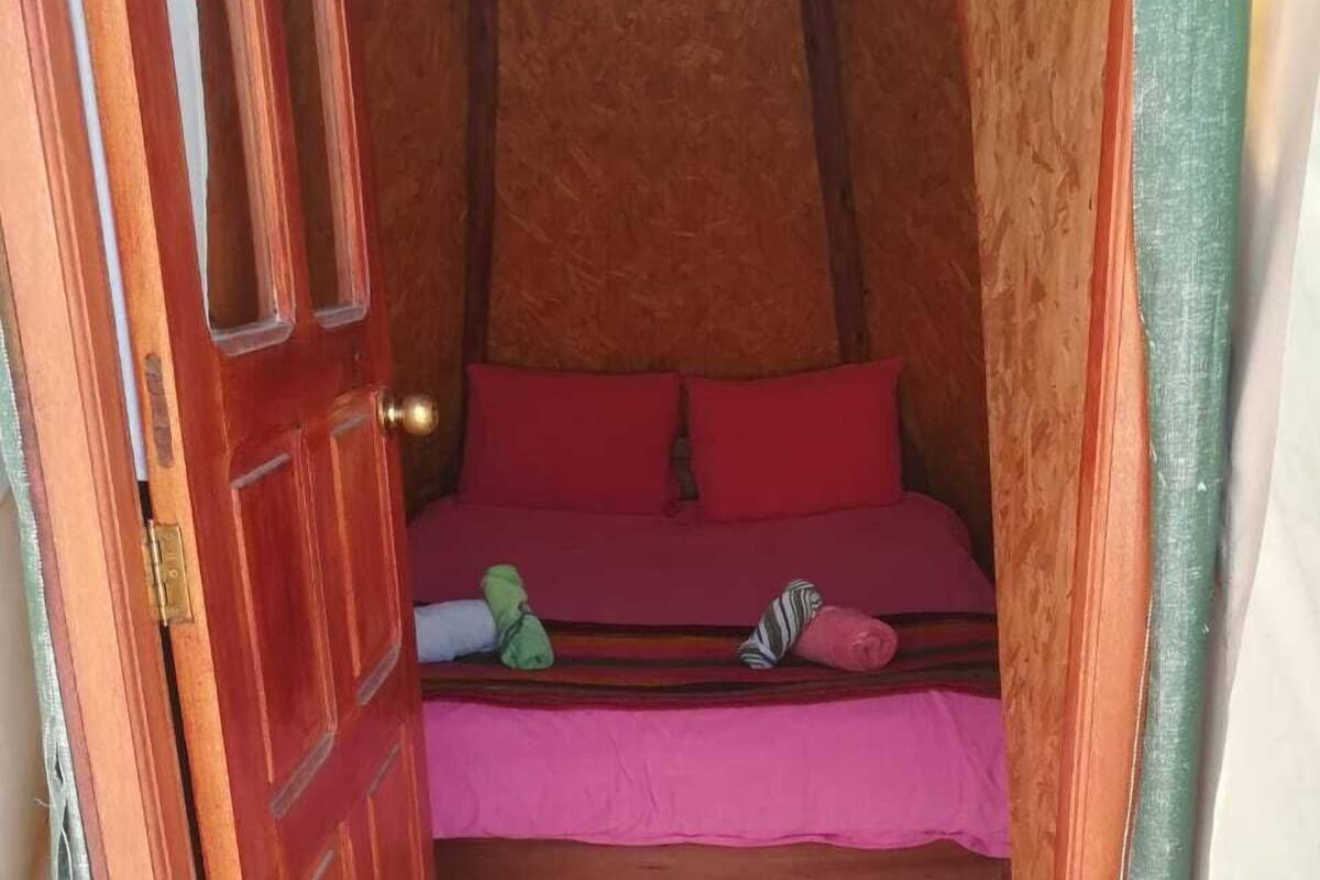 A small, cozy room with a wooden bed, a red mattress, and a green blanket.