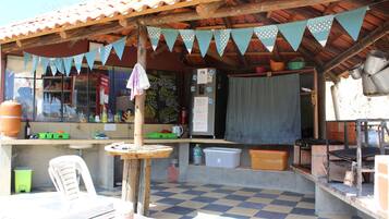 Un café rústico al aire libre con suelo de baldosas, mesas de madera y una barra con varios artículos.