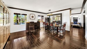 A spacious dining area with a wooden table and chairs, large windows with views of greenery, and decorative wall art.