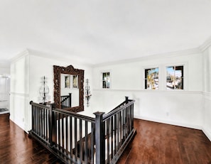 Een ruime kamer met een houten vloer, witte wanden en een zwarte balustrade.