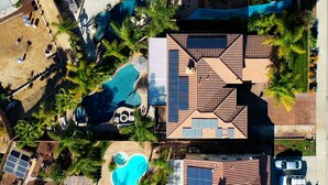 An aerial view of a resort with multiple swimming pools, solar panels, and a large building with a tiled roof.