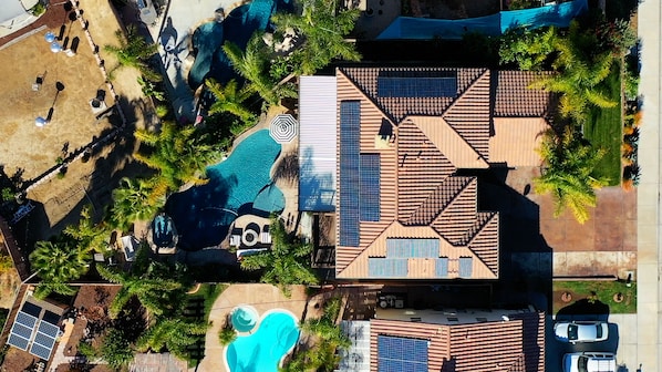 Luchtbeeld van een resort met meerdere zwembaden, zonnepanelen en een groot gebouw met een betegeld dak.