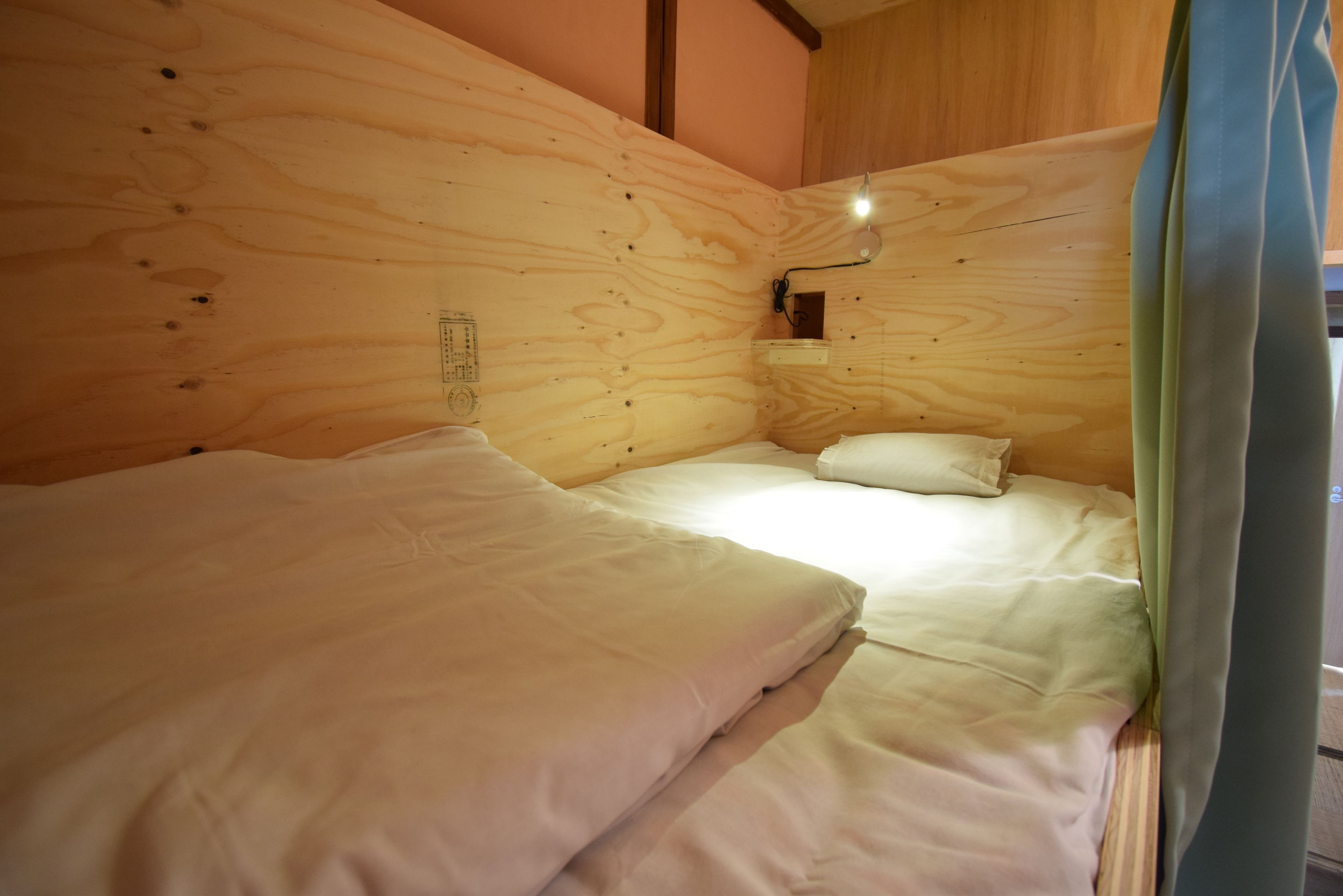 A wooden cabin room with two beds, a wall-mounted light, and a small shelf.