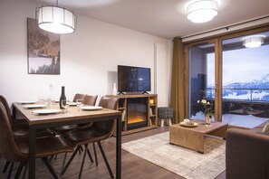 A modern living room with a dining area, a TV, and a large window with a snowy mountain view.