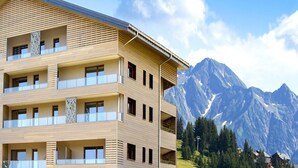 Un edificio de varios pisos con balcones, un paisaje montañoso al fondo y un cielo despejado.