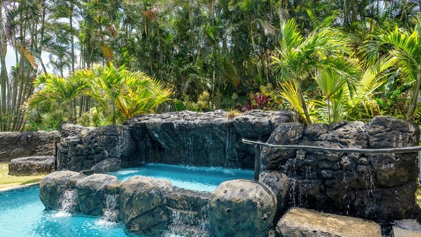Ein Poolbereich mit Wasserfall, umgeben von tropischer Bepflanzung.