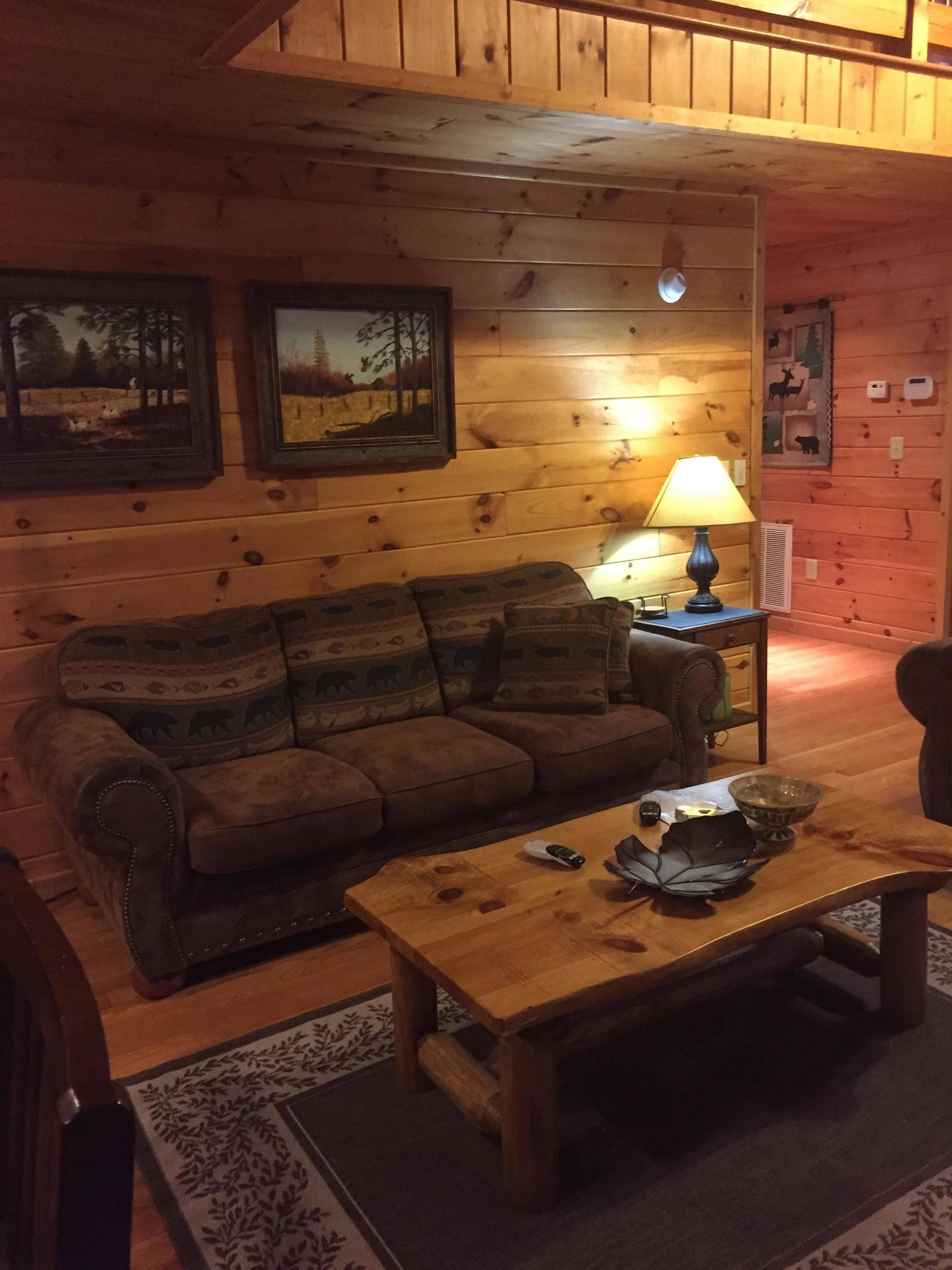 A cozy cabin interior with a wooden ceiling, a sofa, a coffee table, and a lamp.