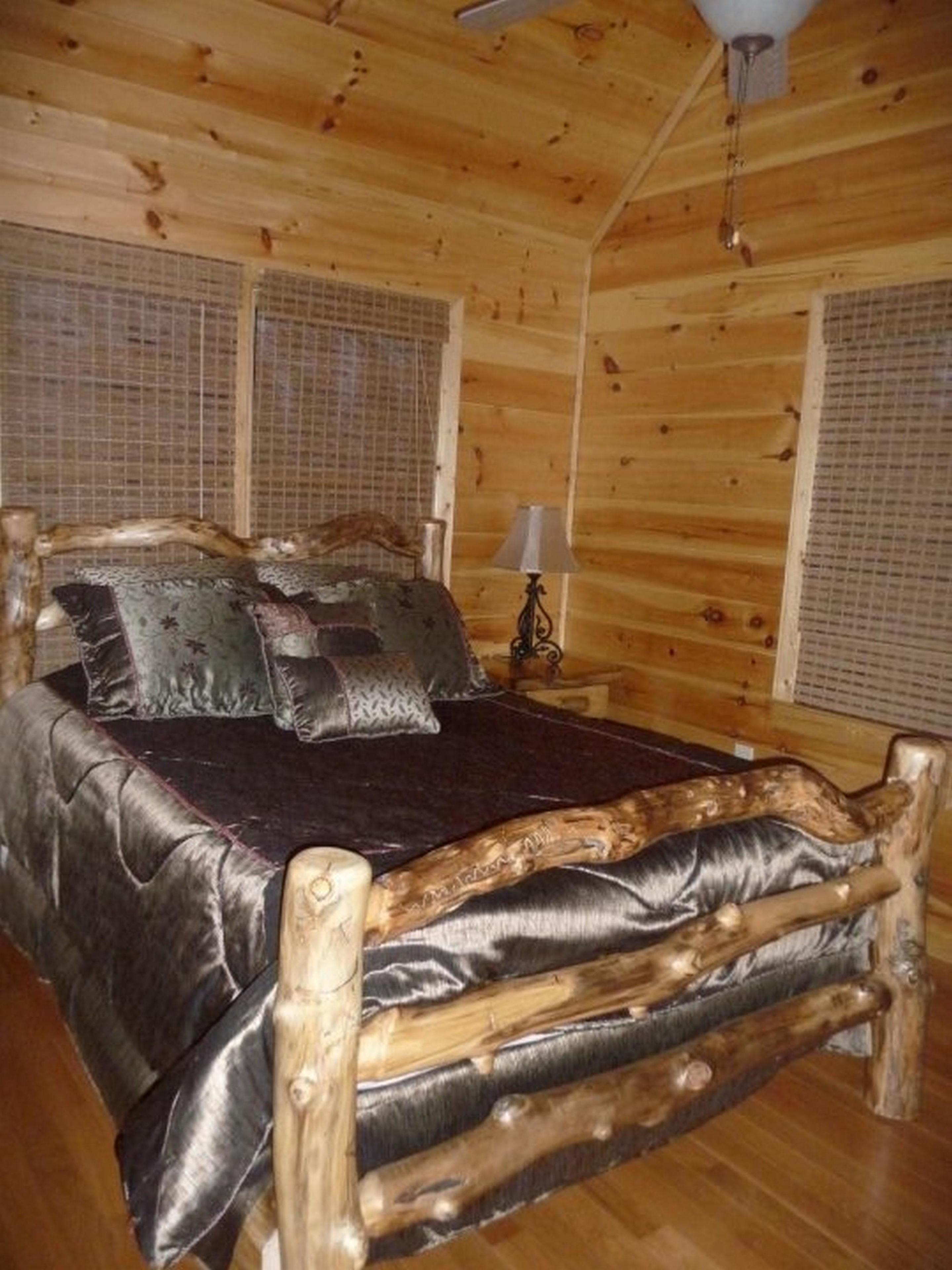 Une chambre dans une cabane en bois, avec un lit, des oreillers, une table de chevet et une lampe.