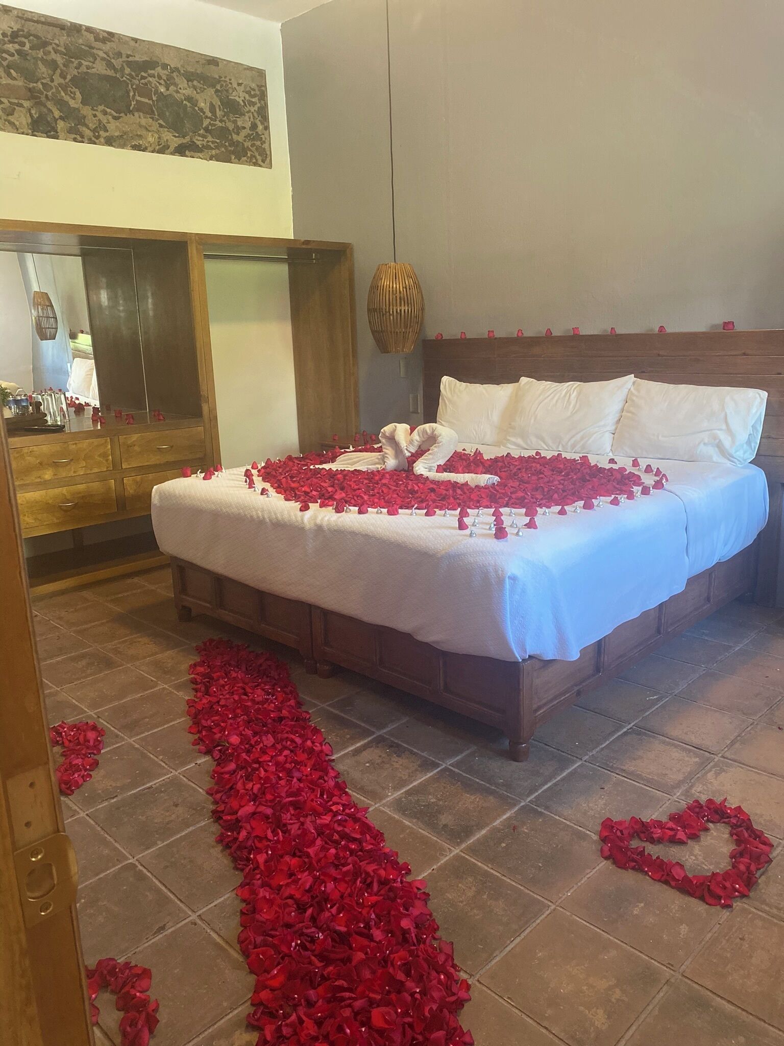 Una cama impecable con sábanas blancas y pétalos de rosa dispuestos sobre la cama y el suelo.