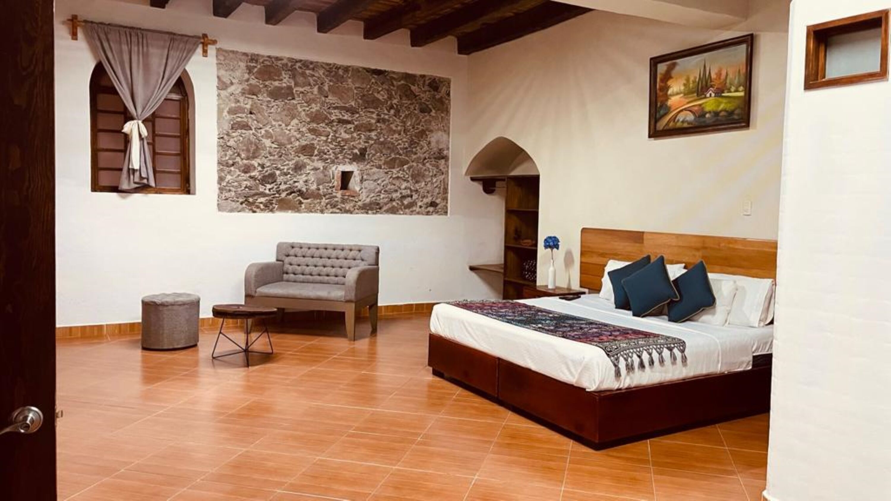A bedroom with a bed, a sofa, a small table, and a stone wall.
