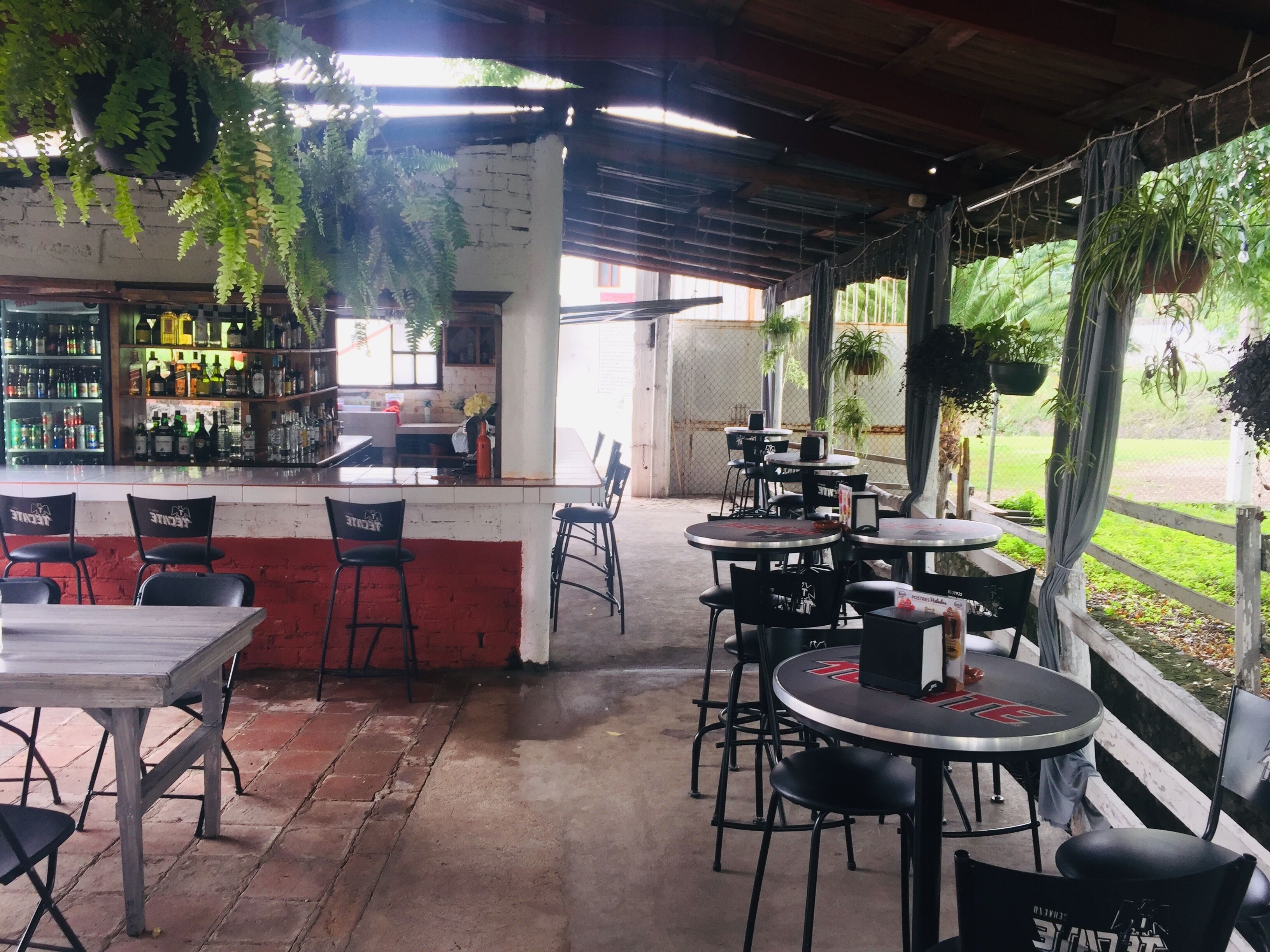 A restaurant with outdoor seating, a bar area, and hanging plants.