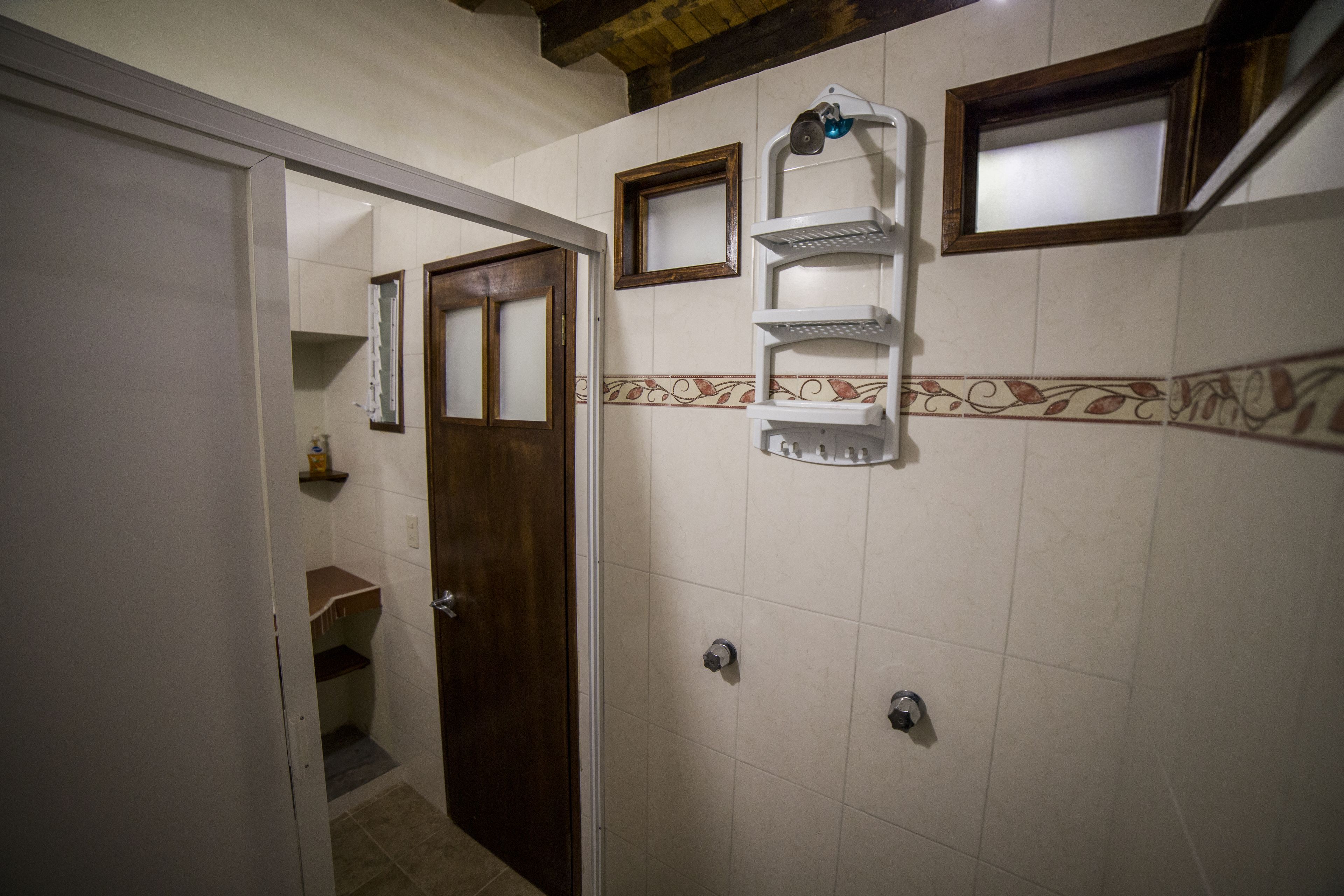 A bathroom with a shower, a door leading to another room, and a shelf with toiletries.
