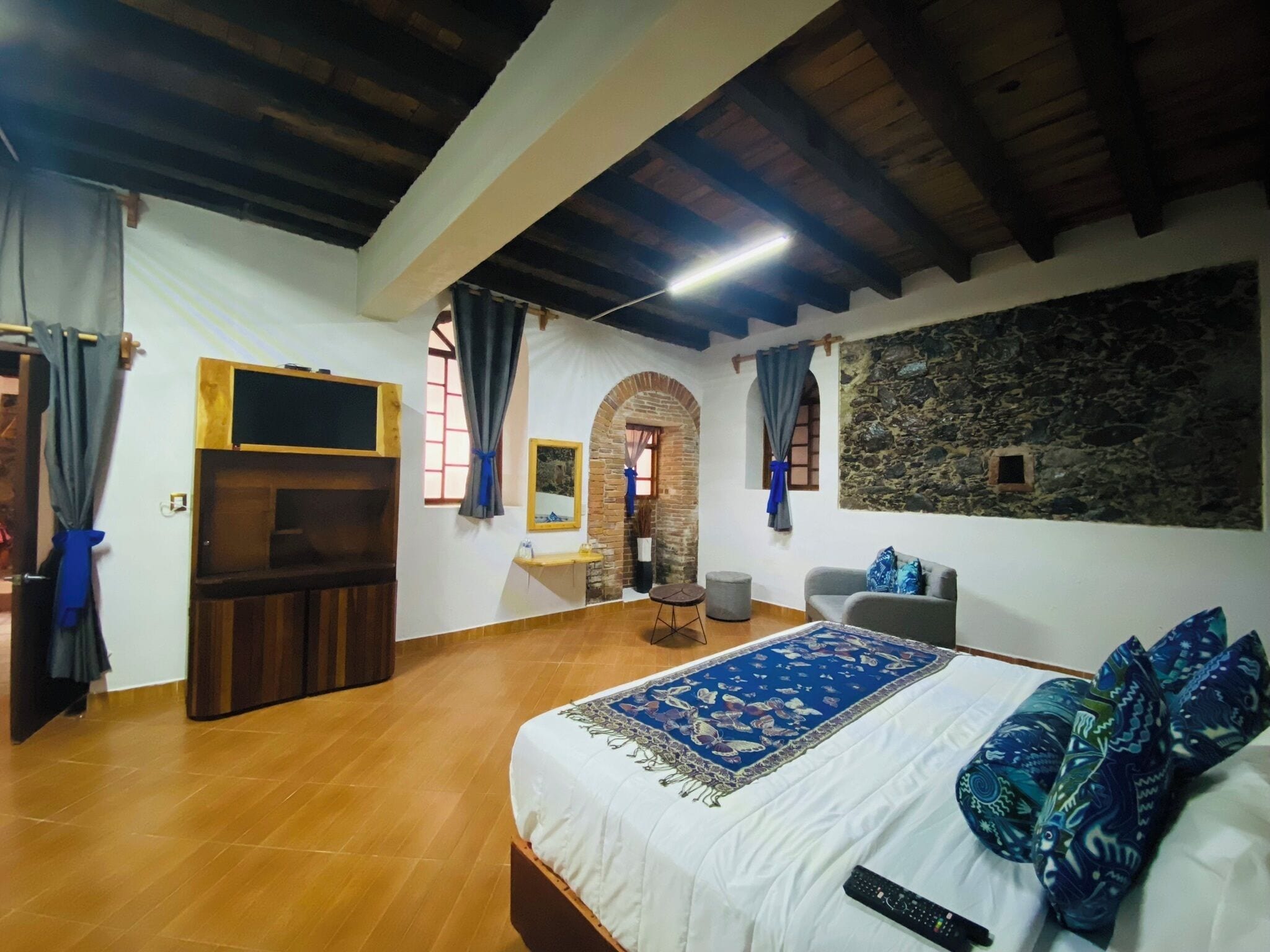 Un dormitorio con cama, televisión, pared de piedra y techo de madera.