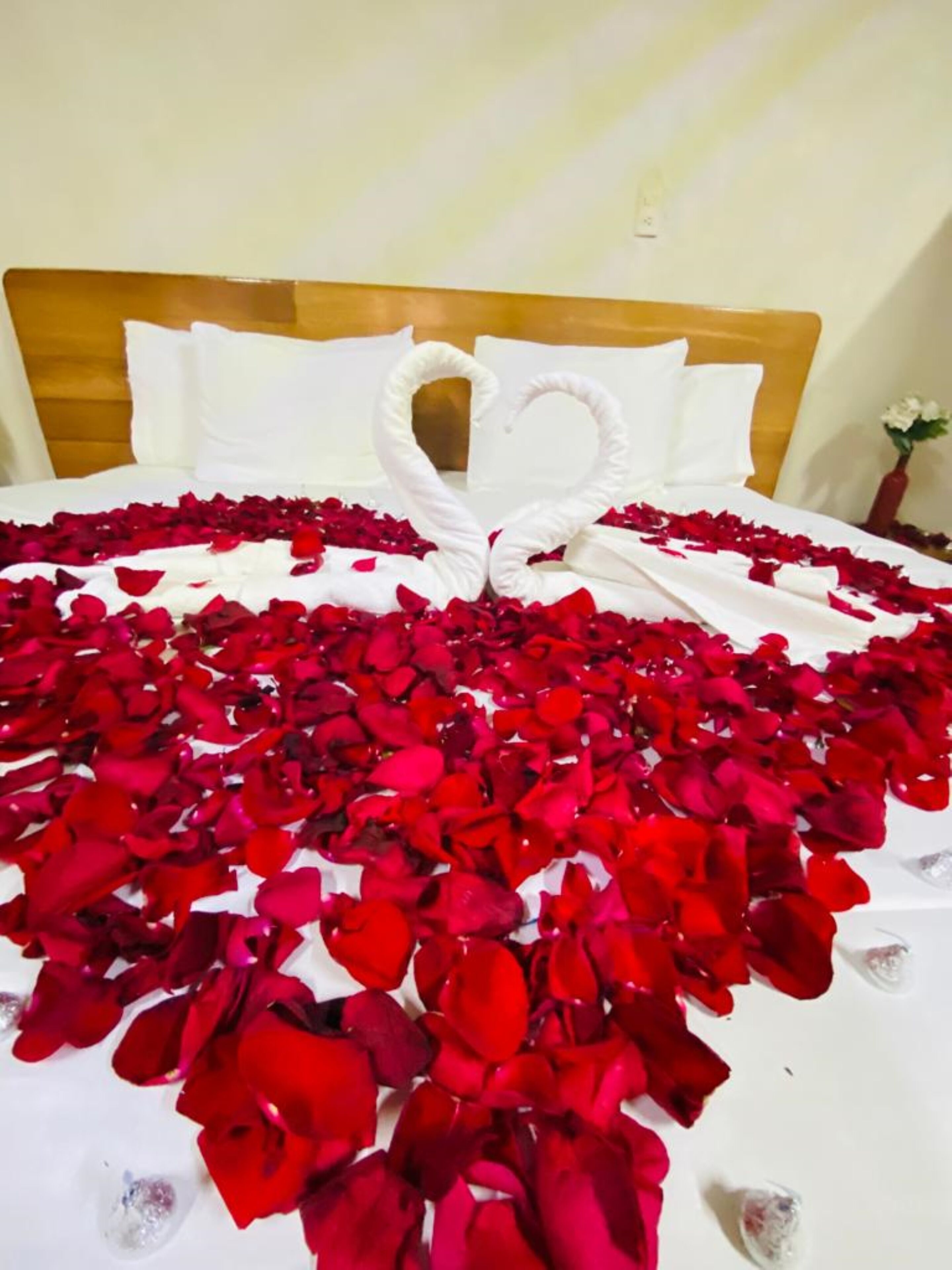 Una cama decorada con pétalos de rosa y dos toallas blancas dispuestas en forma de corazón.