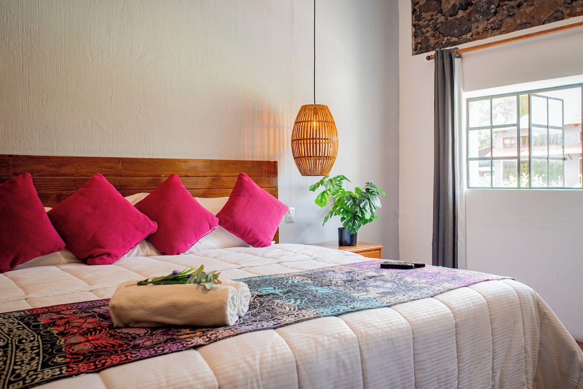 A neatly made bed with a patterned bedspread, a wooden headboard, and several pink pillows.