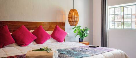 Una cama bien hecha con un edredón estampado, un cabecero de madera y varias almohadas rosas.