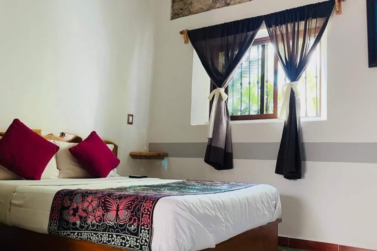 A bedroom with a bed, a chair, and a window with curtains.