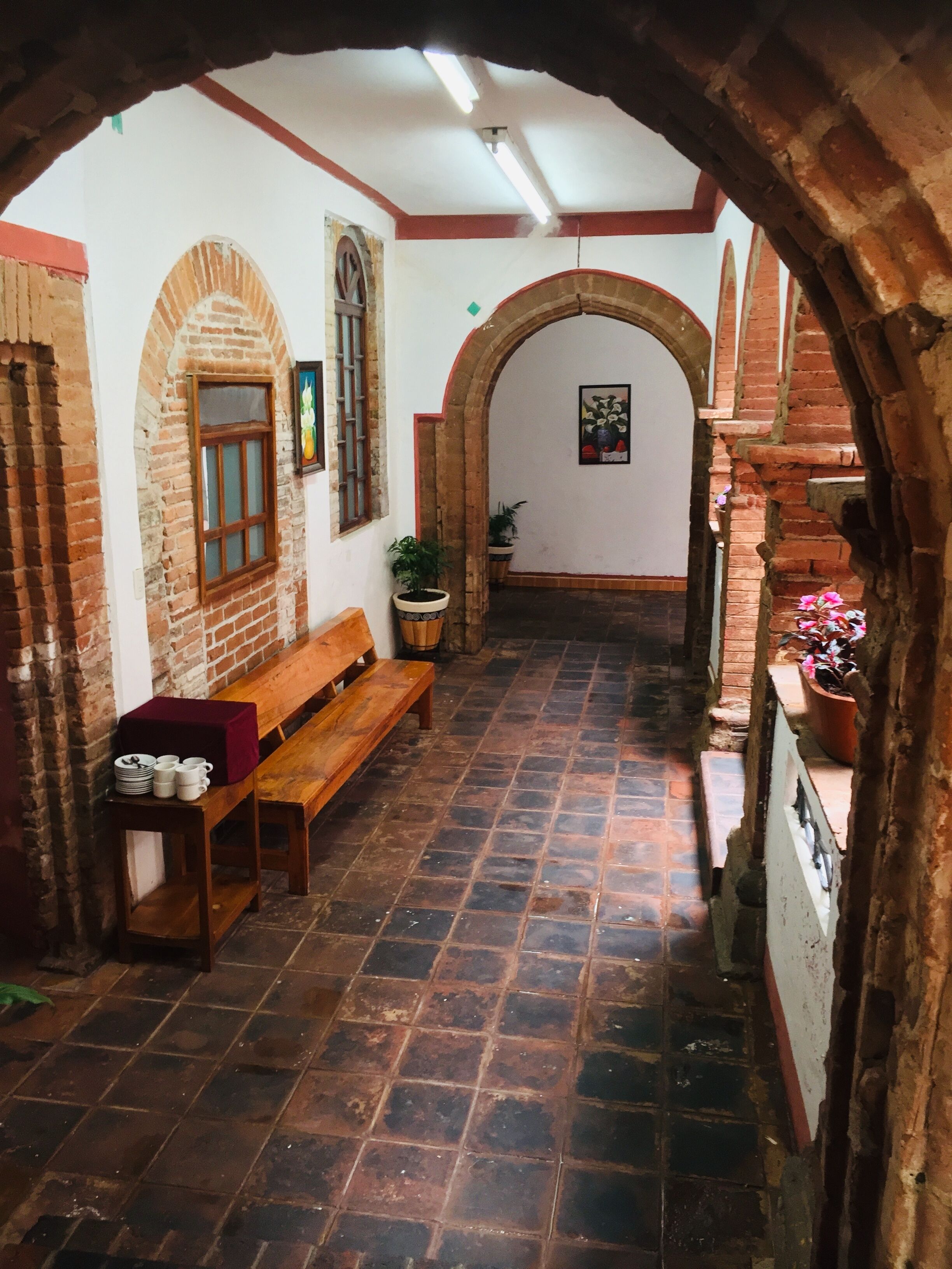 Um corredor estreito com um banco de madeira e plantas em vasos, paredes de tijolo e piso de azulejos.