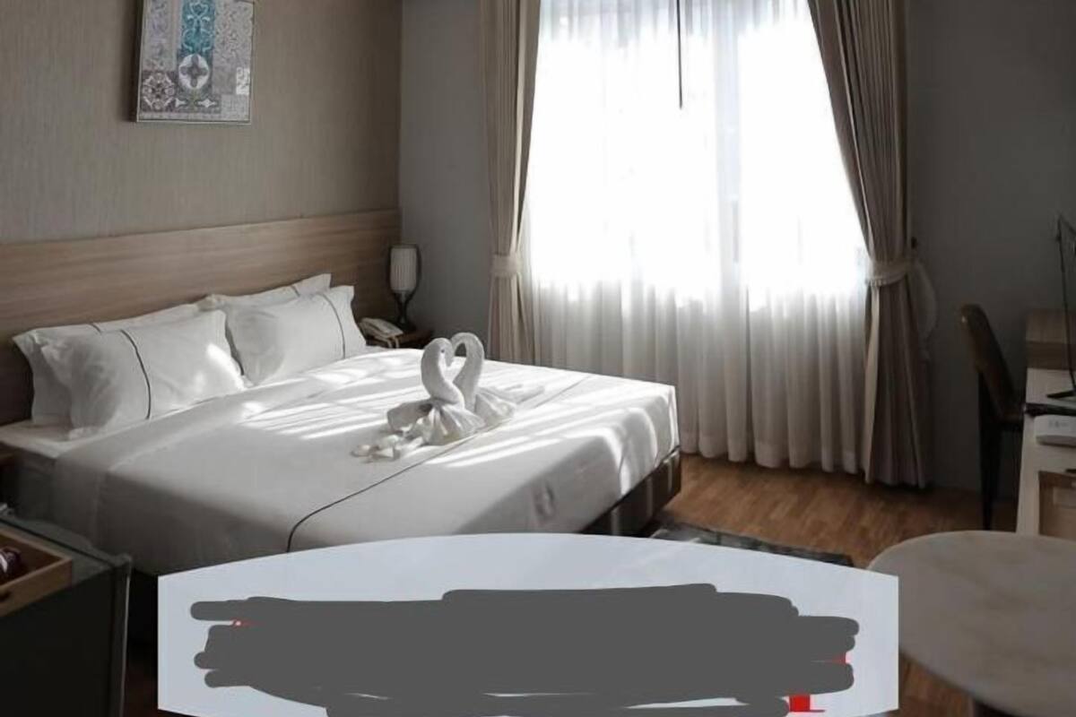 A hotel room with a neatly made bed, a bedside table, a lamp, and a window with curtains.
