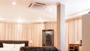 A modern hotel room with a leather sofa, a round coffee table, a bed with white linens, and a large window with curtains. - One Vientiane Hotel & Restaurant (Vientiane)