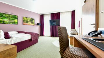 A hotel room with a bed, a desk, a chair, a TV, and a phone.