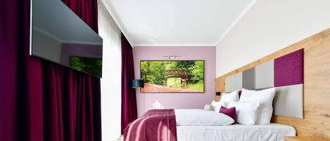 A modern hotel room with a large bed, a view of greenery, and a painting on the wall.