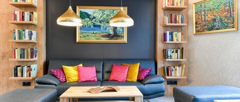 A modern living room with a sofa, ottoman, and coffee table, surrounded by bookshelves and a painting.
