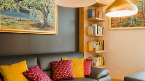 A modern living room with a leather sofa, colorful cushions, a bookshelf, and two paintings on the walls. - Best Western Plus Parkhotel & Spa Cottbus (Cottbus)