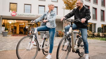 Zwei Personen mit Fahrrädern vor einem Gebäude, an dem ein Schild mit der Aufschrift 'Best Western PLUS' befestigt ist.