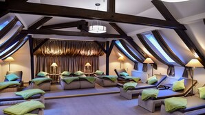 Un cuarto de spa con varias camillas de masaje, toallas verdes y lámparas.