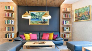 Una sala de estar moderna con un sofá azul oscuro, cojines coloridos, una mesa de centro de madera y estanterías llenas de libros.