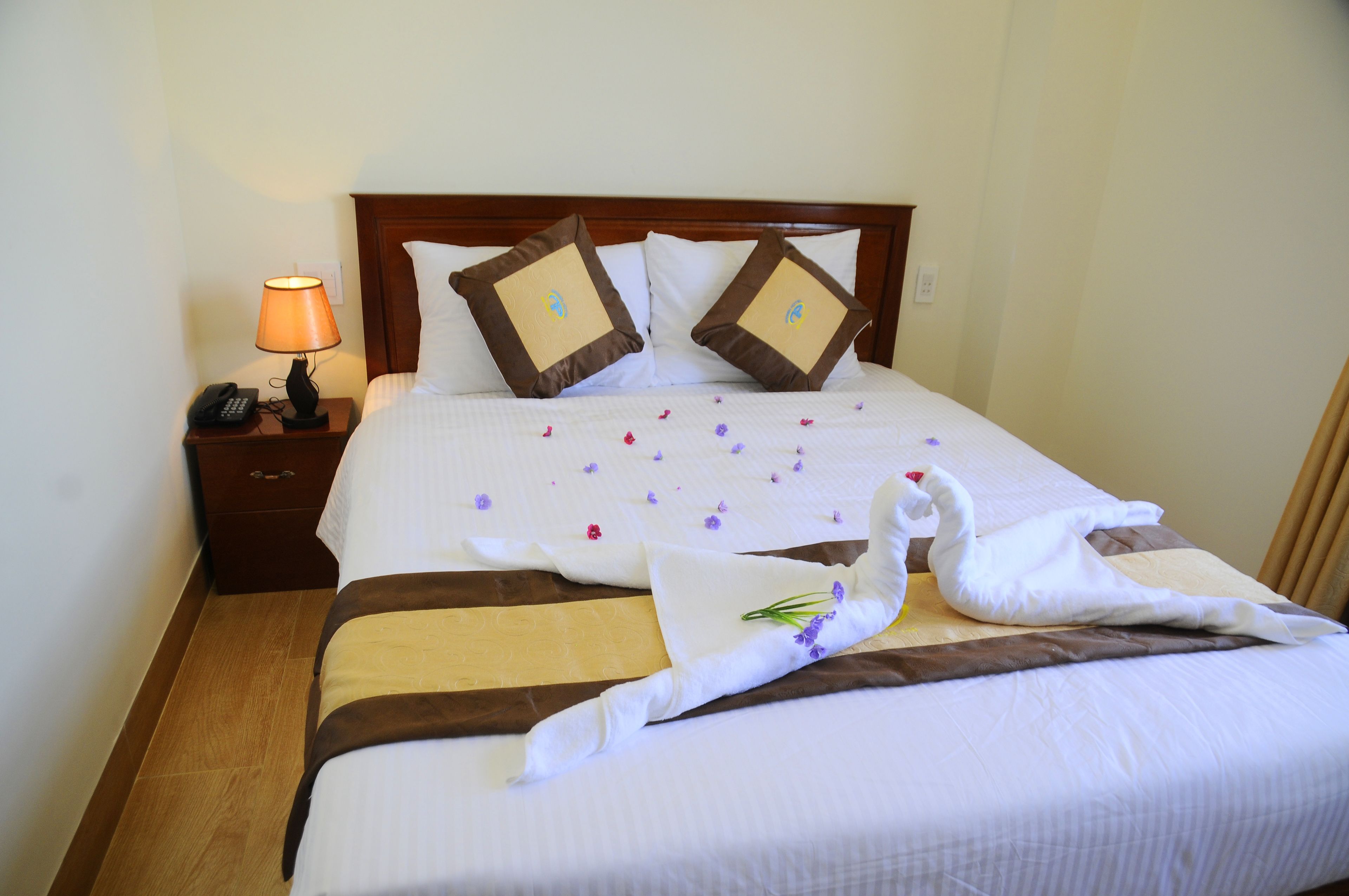 Una cama bien hecha con almohadillas decorativas, una lámpara de noche y un arreglo floral sobre la cama.