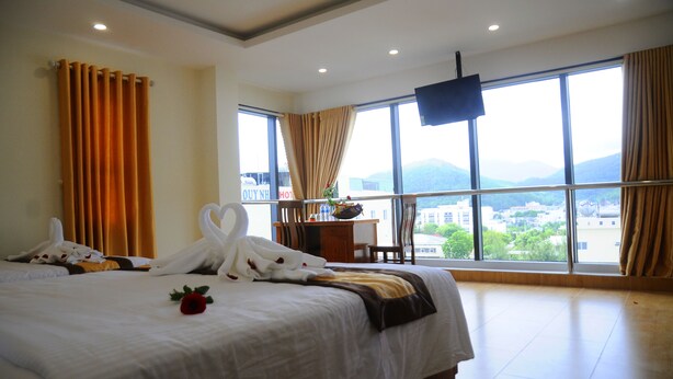 Ein Hotelzimmer mit einem großen Bett, einem Schreibtisch und Blick auf die Stadt durch große Fenster.