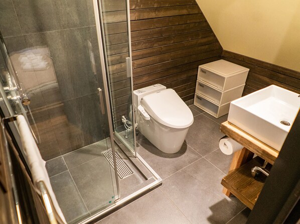 Uma casa de banho moderna com cabine de duche em vidro, sanita branca e lavatório com toucador de madeira.