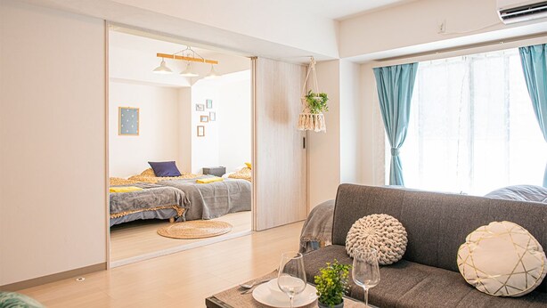 A modern living room with a sofa, a dining table with a plant, and a bed in the background. - LY INN Ryogoku Annex (Tokyo)
