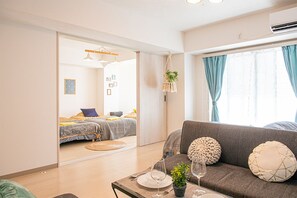 A modern living room with a sofa, a dining table with a plant, and a bed in the background.
