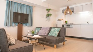 A modern living room with a grey sofa, a dining table, and a kitchen area with white cabinets and a built-in oven. - LY INN Ryogoku Annex (Tokyo)