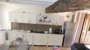 A compact kitchen with white cabinets, a microwave, and a sink. There's a dining table with chairs and a colorful striped cushion. - Charming apartment between sea and mountains (Sollacaro)