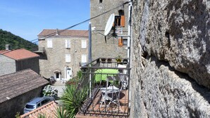 A stone building with a tiled roof, a balcony with metal railings, and potted plants. - Charming apartment between sea and mountains (Sollacaro)