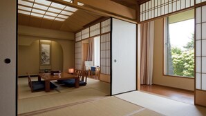 A traditional Japanese room with tatami flooring, sliding shoji doors, a low table with cushions, and a view of greenery outside. - KIYOSATO KOGEN RESORT (Hokuto)