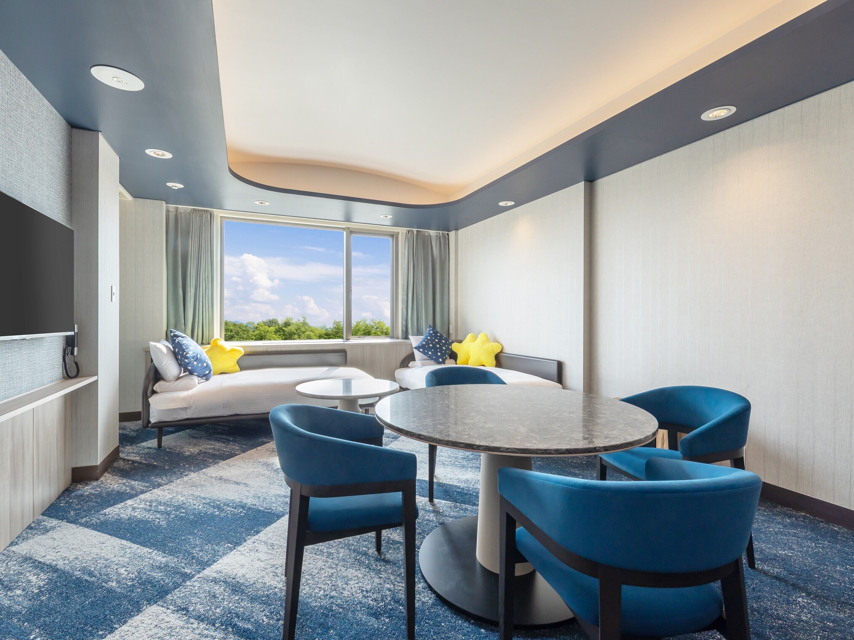 Une chambre d’hôtel avec une grande fenêtre, un canapé, une table ronde et quatre chaises.