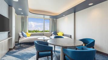 Une chambre d’hôtel avec une grande fenêtre, un canapé, une table ronde et quatre chaises.