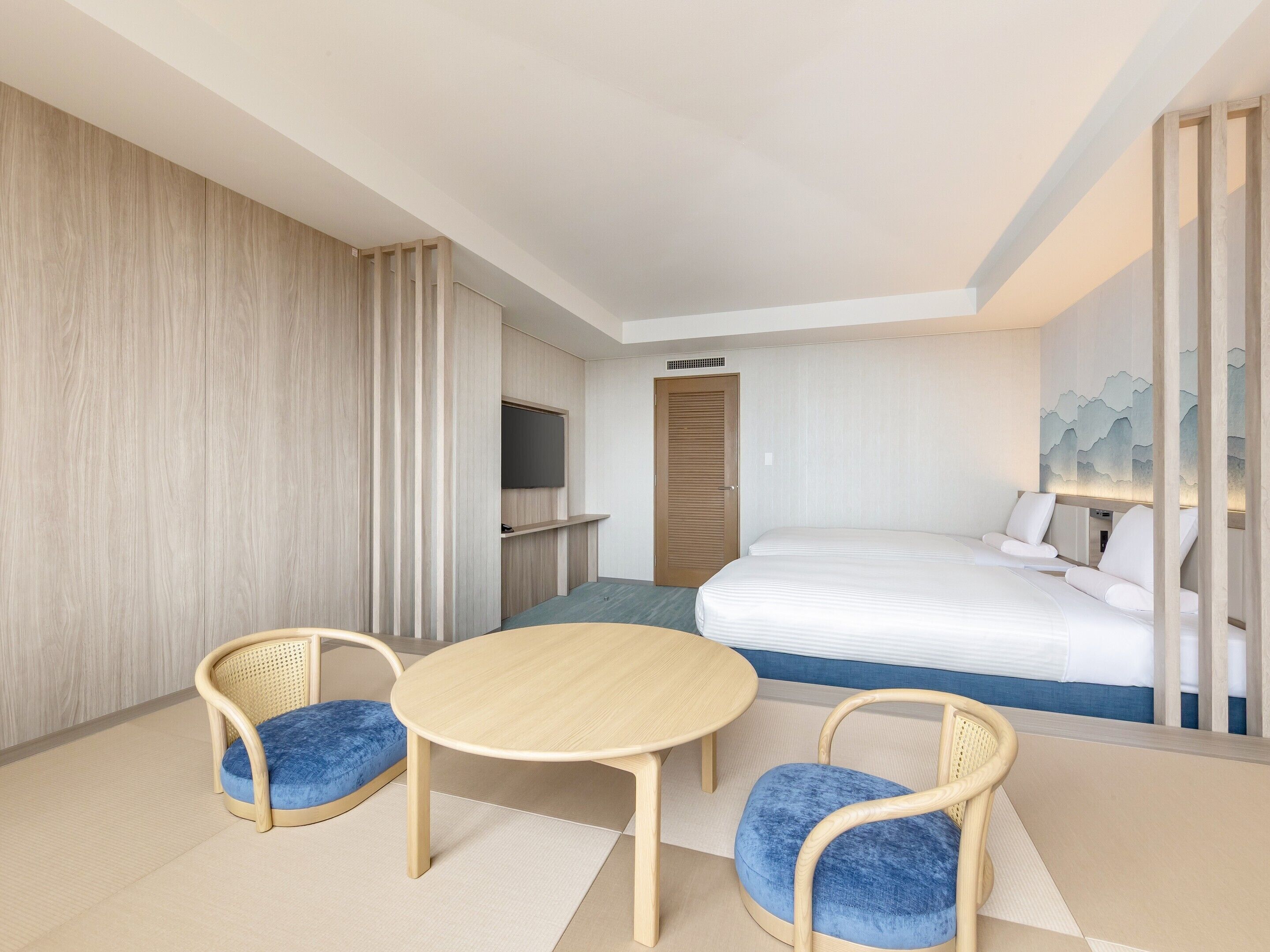 A hotel room with a bed, a desk, two chairs, a television, and a door.