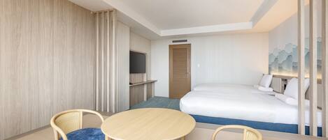 A hotel room with a bed, a desk, two chairs, a television, and a door.