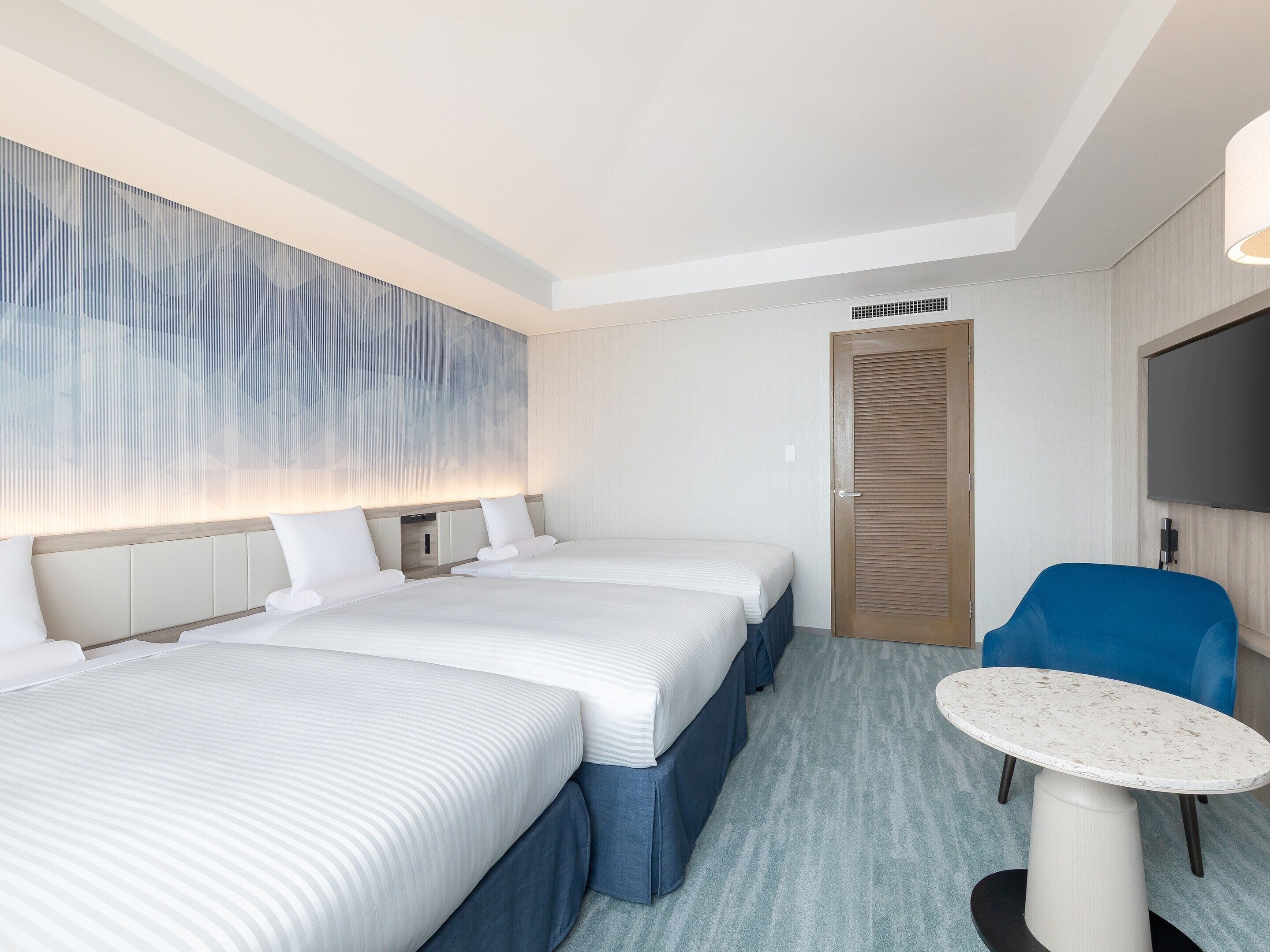 A hotel room with two beds, a TV, a desk, and a door.