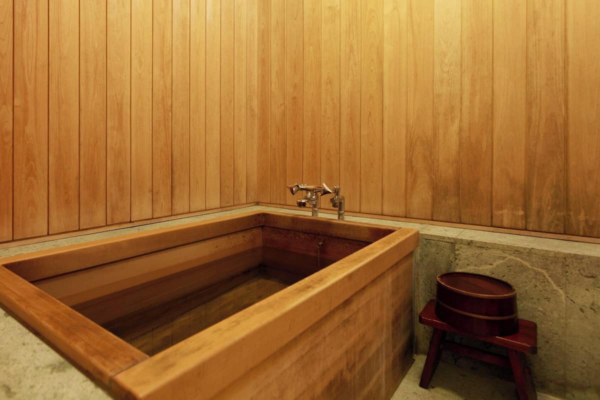 A wooden bathtub with a faucet, a wooden bench, and a stone wall.