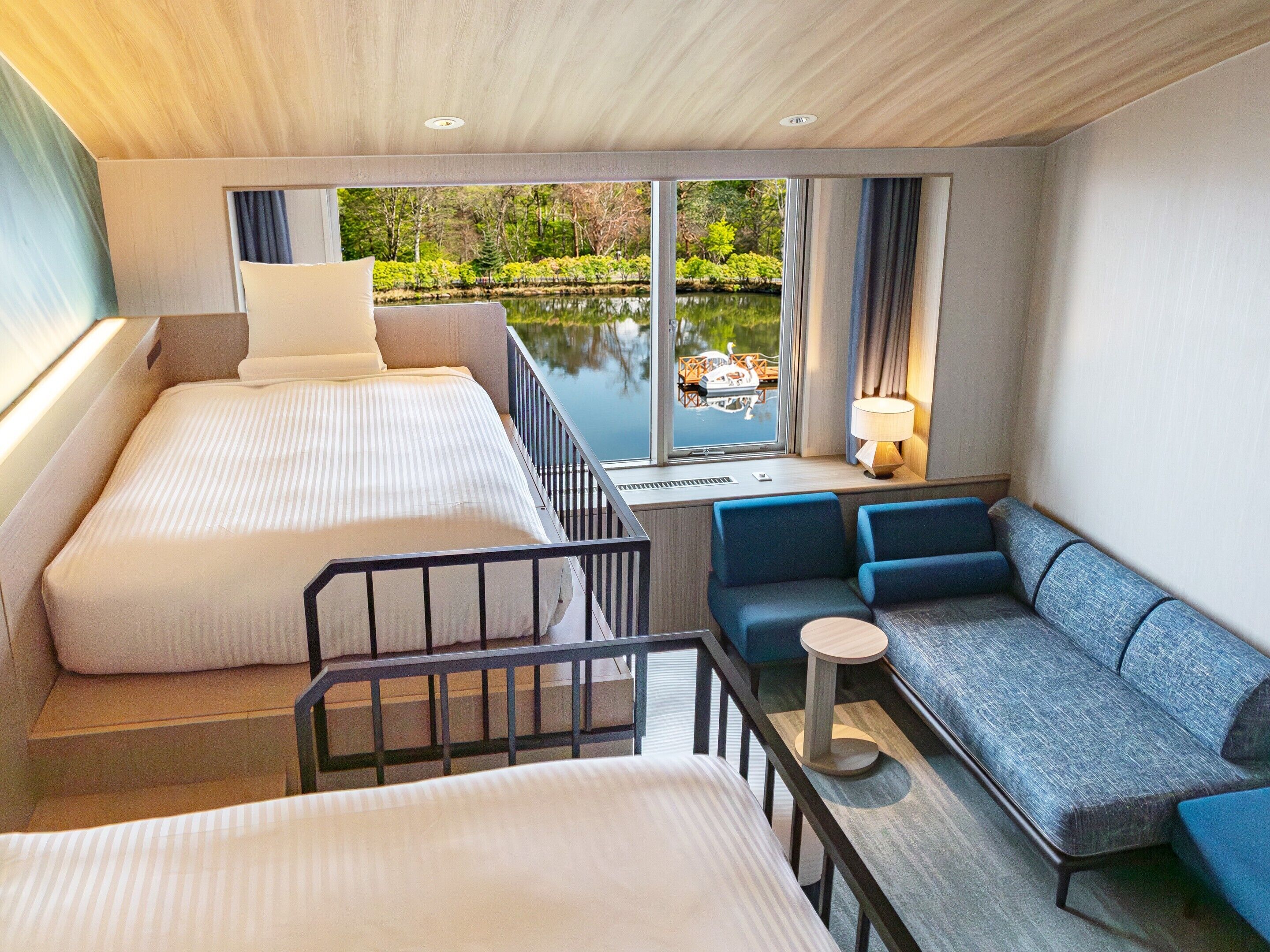 Quarto de hotel com uma cama, um sofá, uma mesa pequena e vista para um lago.