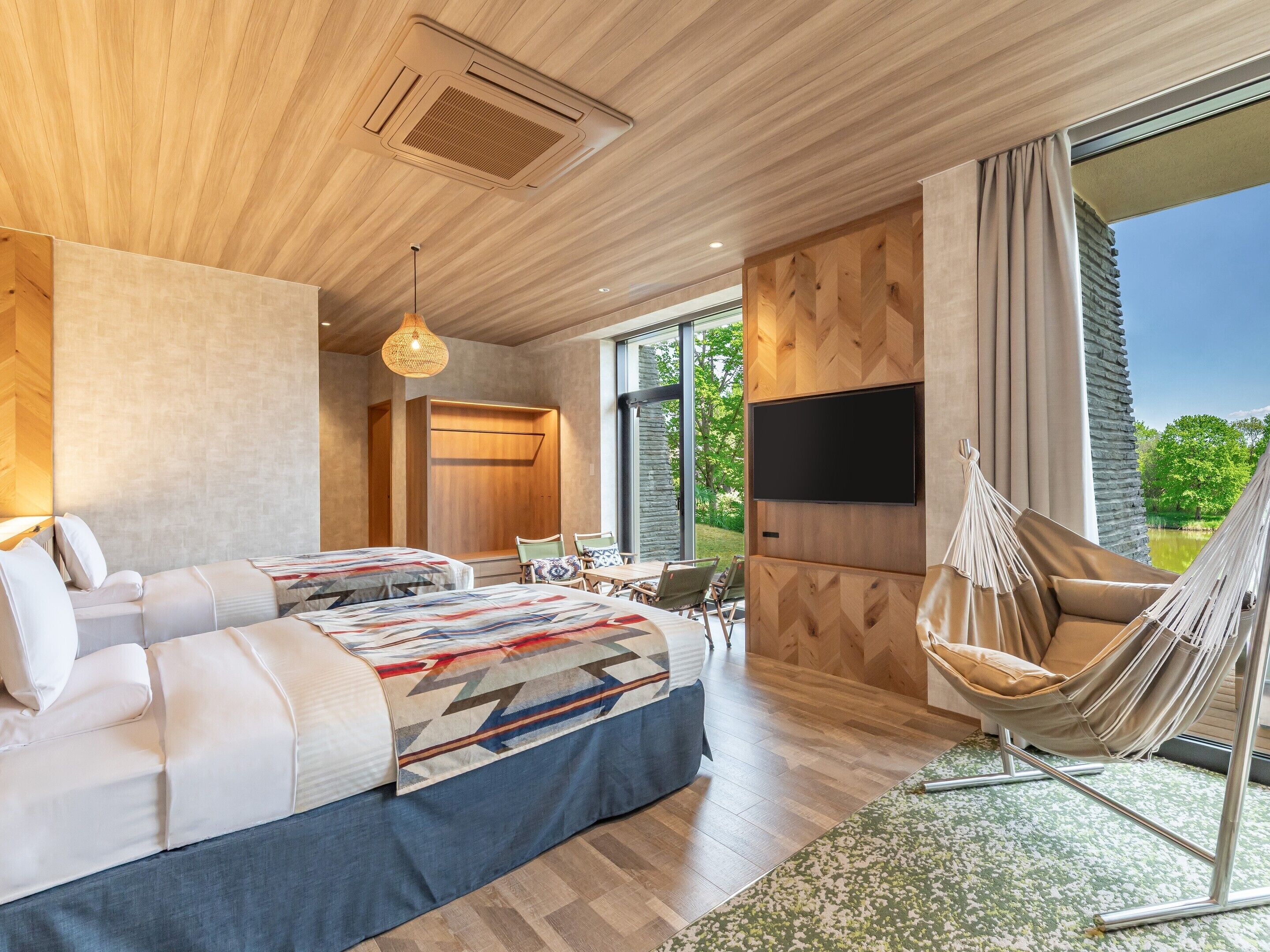 A modern hotel room with a large bed, a TV, a hammock, and a view of the outdoors.