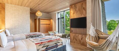 A modern hotel room with a large bed, a TV, a hammock, and a view of the outdoors.