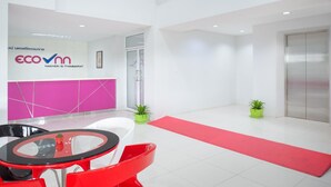 A modern lobby with a reception desk, a glass table, red chairs, potted plants, and a red carpet. - Eco Inn Lite Nakhon Si Thammarat (Nakhon Si Thammarat)